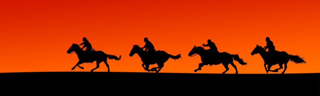 Panoramic silhouette of four horses and riders at sunset.